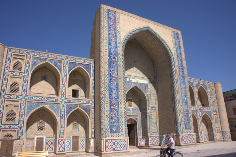 Historic Bukhara Madrasa building with intricate blue tilework and grand archways.